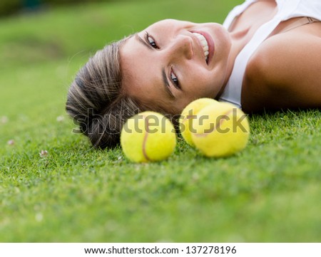 Female tennis player lying on the lawn with balls