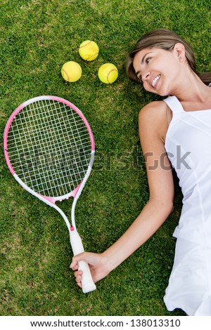 Female tennis player lying on the floor with racket and balls