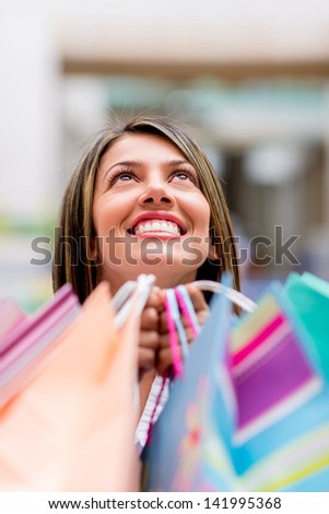 Happy female shopper looking up and holding bags