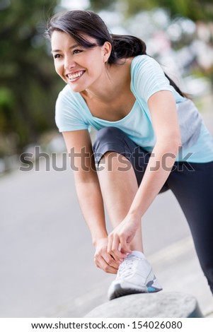 Happy female runner tying her shoelace outdoors