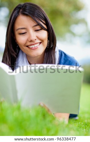 Beautiful woman lying outdoors on the grass and reading a book