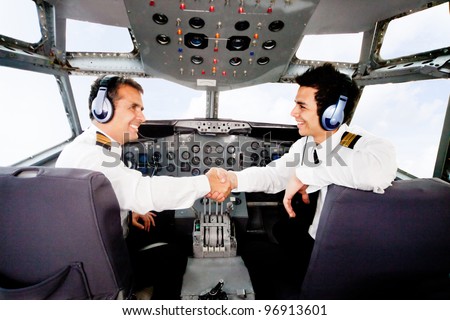 Happy pilots handshaking in the airplane cabin