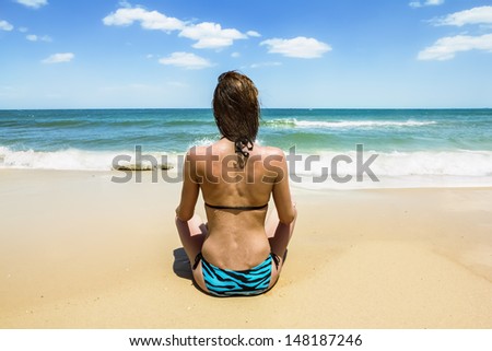 Tanned girl in bikini sitting on the beach and looking at the horizon