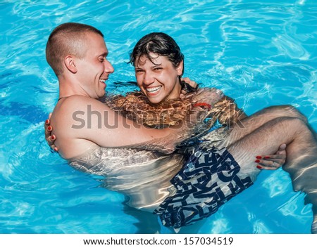 A girl holds a guy in her arms while standing in the pool