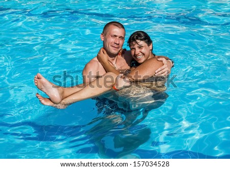Guy holds a girl on hands while standing in the pool