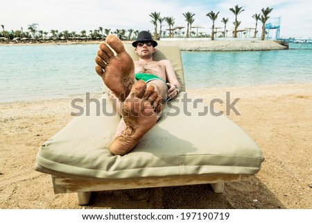 The man in the hat sunbathes on a lounge chair on the beach at a resort in sunny day