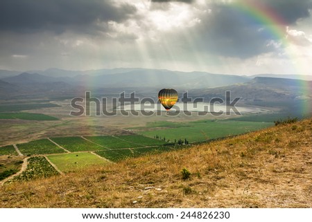 The balloon is flying over the Valley near the village of Koktebel in Crimea against the backdrop of the dramatic sky with a rainbow