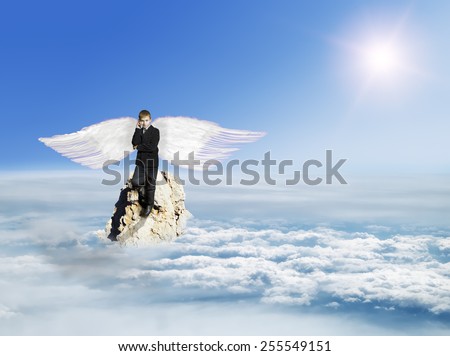 The boy with the phone in the costume with Angel Wings on a rock in the sky above the clouds