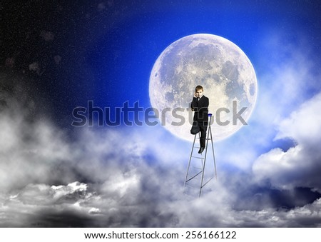 Boy in suit stands on a step-ladder against the background of a full moon and a starry sky