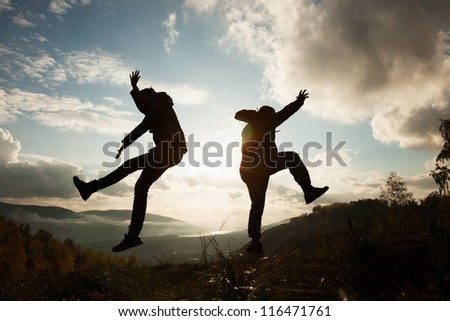 silhouettes young woman and man jumping at the sunset