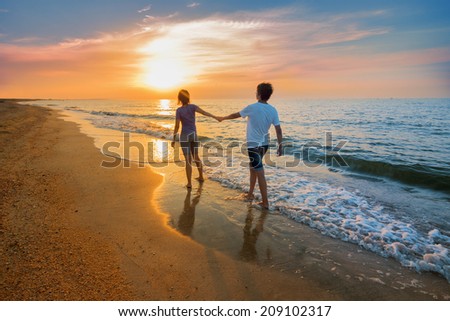 Boy and girl go on the beach during sunset