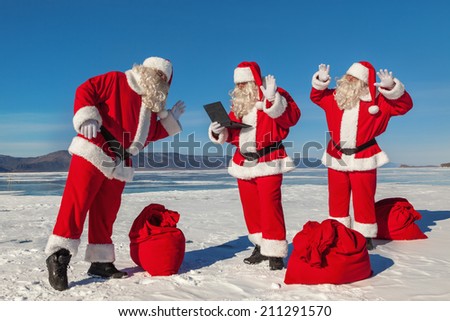 Three Santa Claus talking to someone on the Internet in winter, multiexposition, shooting was conducted in a sunny day on lake Baikal