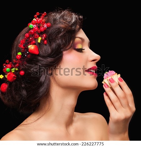 Beautiful young woman with evening make-up in the style of the summer eating tasty cake on a black background