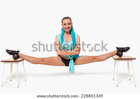 A girl sits in a pose of twine between two stools on a white