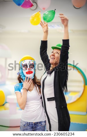 Sad girl in clown mask and cheerful woman at a children\'s party