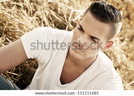 Portrait of  a beautiful young man outdoors in white casual shirt aitting on hay field