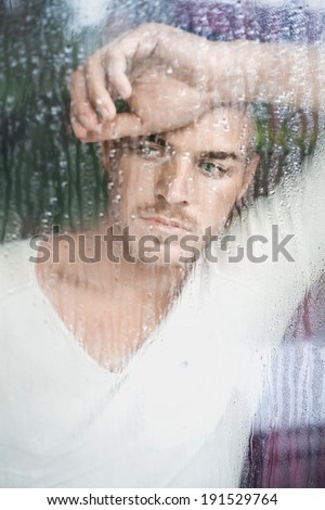 Closeup portrait of handsome young man looking through wet window