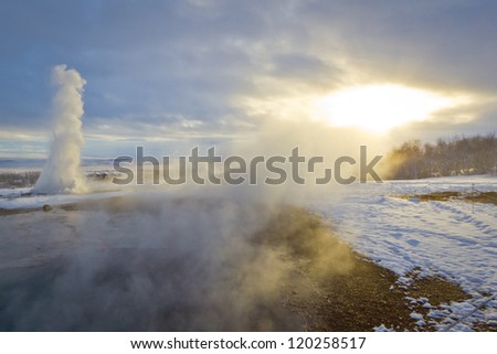 Konungshver geyser steams towards the sun, while Strokkur geyser erupts in the background, in Iceland
