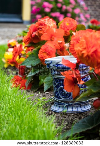Ceramic Pot in Garden.  A blue china ceramic pot with an angry man face nestled in salmon red begonia flowers in a cultivated garden.