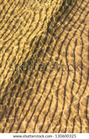 A small wave rolls over rippled sand on a sunny sandy beach