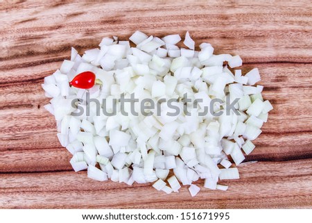 Freshly CHopped Onion with a Red Chili.  A large pile of freshly diced white onion on a wooden chopping board, with a single red chili