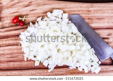 Diced White Onion with Red Chillis and kitchen knife.  A fresh pile of chopped white onion garnished with two red chillis, with chef\'s knife and wooden chopping board