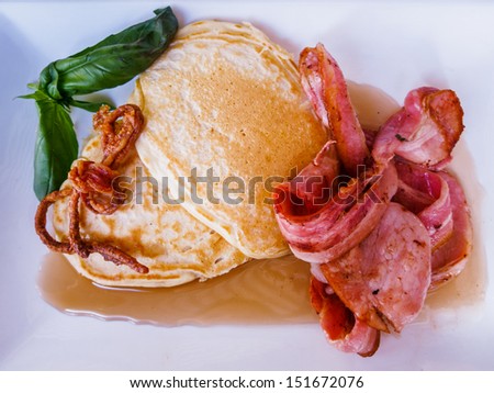 Buttermilk Pancakes with Bacon Rashers and Maple Syrup. Hot fresh bacon, pancakes in maple syrup, garnished with a tie of fried bacon rind and fresh green basil leaves