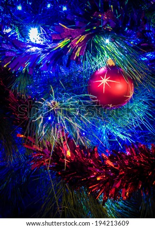 Close up of a brightly decorated Christmas tree, with glittering tinsel, shiny red ball, and fairy lights