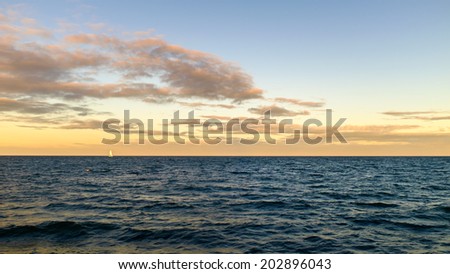 A sailboat sailing on the open ocean catches the last rays of the golden sun as the sun sets