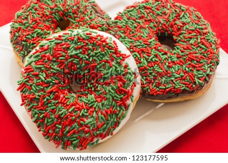 Three vanilla and chocolate covered doughnuts with red and green sprinkles on white plate and red tablecloth