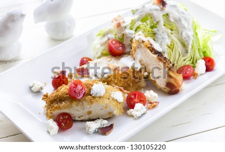 Salad of iceberg lettuce wedge with breaded chicken, cherry tomatoes, bacon and blue cheese crumbles, drizzled with herb buttermilk dressing