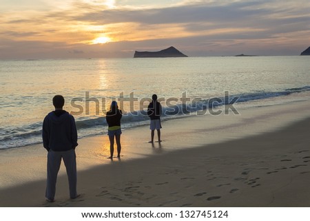 Three people starting the day appreciating a beautiful sunrise at Waimanalo Bay in Oahu, Hawaii