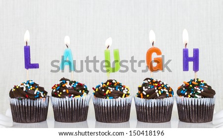 Lit multicolored candles that spell LAUGH in chocolate mini cupcakes with colored sprinkles