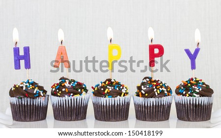 Lit multicolored candles that spell HAPPY in chocolate mini cupcakes with colored sprinkles