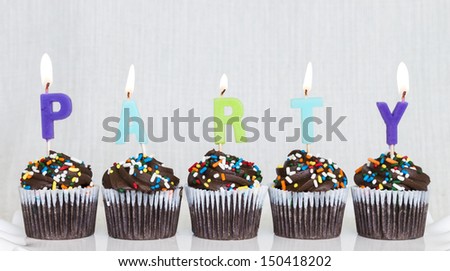 Lit multicolored candles that spell PARTY in chocolate mini cupcakes with colored sprinkles