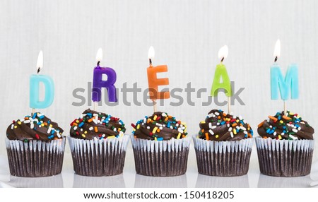 Lit multicolored candles that spell DREAM in chocolate mini cupcakes with colored sprinkles