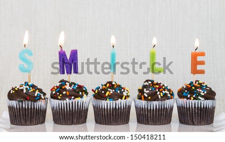 Lit multicolored candles that spell SMILE in chocolate mini cupcakes with colored sprinkles