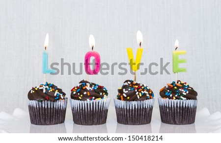 Lit multicolored candles that spell LOVE in chocolate mini cupcakes with colored sprinkles