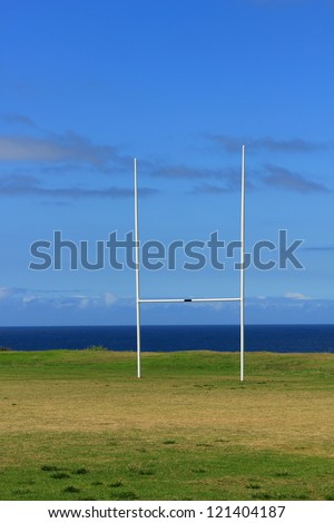 Rugby goalposts. Sports field with white uprights contrasting with the blue sea and blue sky background.\
\
Sports field with a blue sky and blue sea background