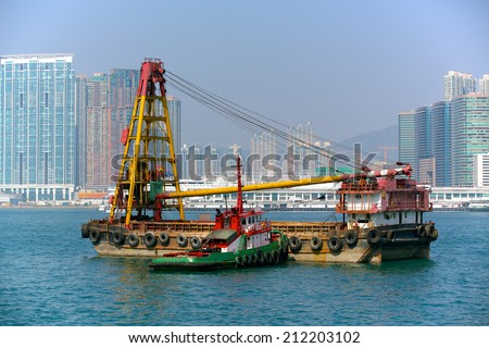 HK Harbor Crane. Scene from Hong Kong harbor, crane used for transferring ship cargo being moved by a tug boat.