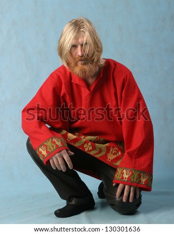 portrait of a man with a red beard and mustache and long blond hair in a red shirt sitting on the floor