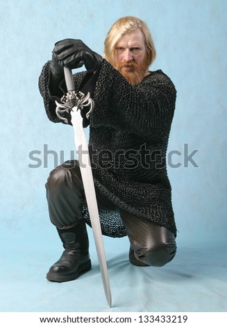 portrait warrior man with a beard and a mustache with a sword in chain mail on a light background crouched