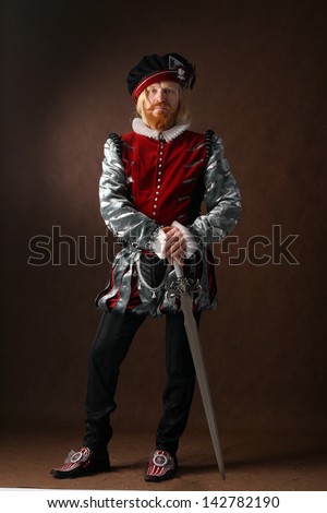 close-up portrait of a man of the Middle Ages with a beard and mustache in a suit isolated on a dark background with a sword standing