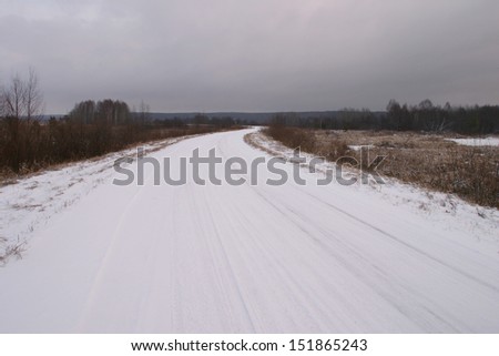 landscape of snow-covered road near the woods at the beginning of winter