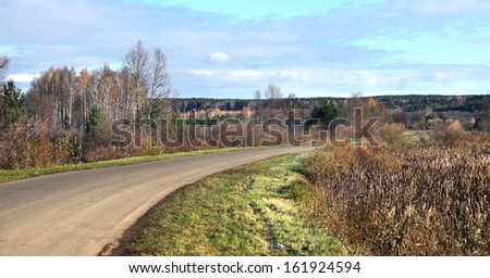 autumn landscape of desert road near the forest and frost on the grass on a cold morning
