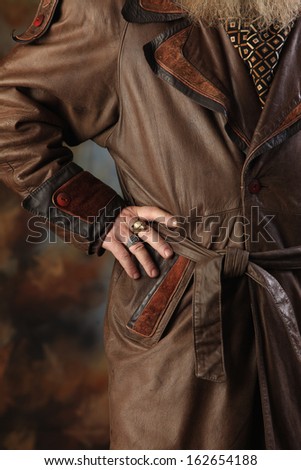 close-up cropped image of a man\'s brown leather coat and his hands on his belt Studio
