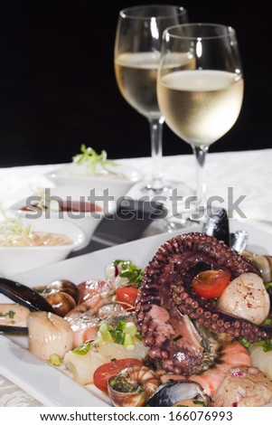 Macro still life white dish with seafood and wine glasses with white wine on a white tablecloth in a studio on a black background