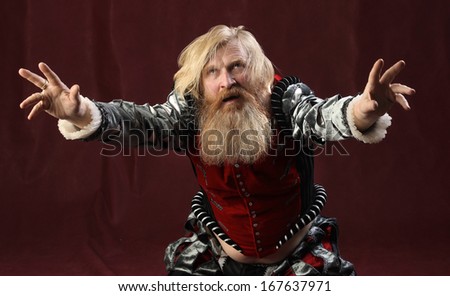 portrait of a man of the Middle Ages with a long beard and mustache, wearing a suit, waving his hands, serious look, studio shot on a burgundy background