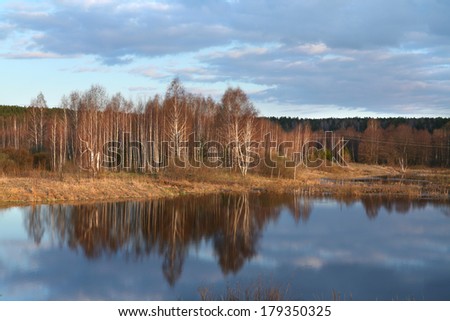 Early spring landscape at the river reflection of bare trees in calm water in the early morning