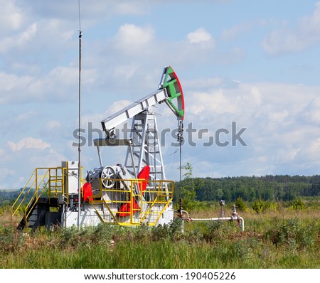 summer landscape oil pump in a green field, cloudy sky above him and the forest on the horizon